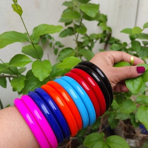 May include: A stack of colorful plastic bangles in pink, blue, orange, light blue, red, and black.