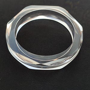 Puede incluir: Brazalete de acr&iacute;lico transparente y facetado. El brazalete tiene un dise&ntilde;o geom&eacute;trico hexagonal. El material transparente permite el paso de la luz, creando un efecto brillante. Un accesorio elegante.