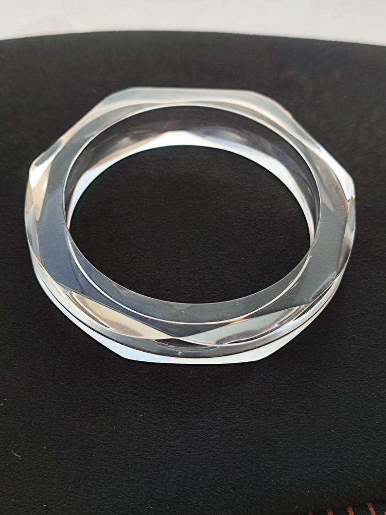 Puede incluir: Brazalete de acr&iacute;lico transparente y facetado. El brazalete tiene un dise&ntilde;o geom&eacute;trico hexagonal. El material transparente permite el paso de la luz, creando un efecto brillante. Un accesorio elegante.