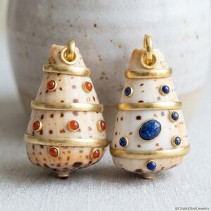 May include: Two cone-shaped shell pendants featuring gold-toned metal bands and inlaid gemstones. The left pendant has orange stones, while the right pendant features blue stones. Each piece includes a circular metal loop at the top for hanging.