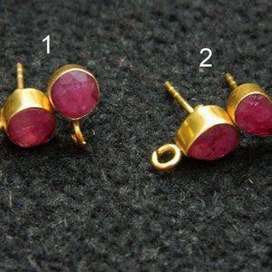 Puede incluir: Dos pares de cierres de pendientes de tono dorado con acentos de piedras preciosas rojas. El primer par presenta piedras preciosas redondas, mientras que el segundo par presenta piedras preciosas en forma de lágrima.