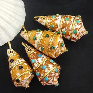 May include: Four seashell pendants with gold-colored metal accents and colorful gemstones. The shells are brown and white, with gold bands and turquoise, green, and black stones. A large white seashell is in the background.
