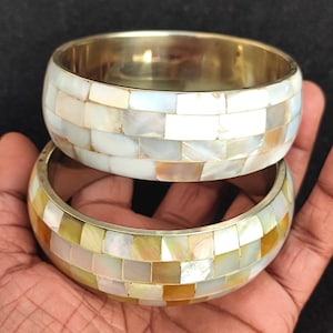 May include: Two silver bangles with a mosaic design made of white and gold mother of pearl tiles.