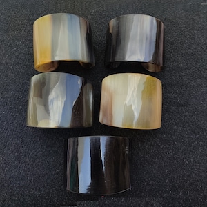 Op de afbeelding: Vijf hoornarmbanden in verschillende tinten bruin en zwart. De armbanden zijn gemaakt van gepolijst hoorn en hebben een glad, afgerond oppervlak.