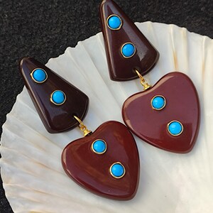 May include: A pair of dangle earrings with a maroon heart shape and a maroon triangle shape. Each shape has three turquoise blue stones.