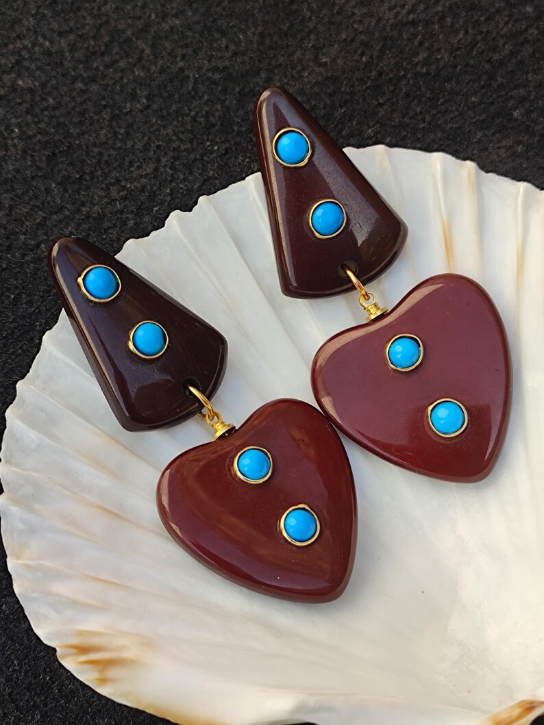 May include: A pair of dangle earrings with a maroon heart shape and a maroon triangle shape. Each shape has three turquoise blue stones.