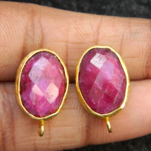 Può includere: Un paio di orecchini ovali con montatura dorata e una pietra preziosa rosa scuro. Gli orecchini hanno un design semplice e sono perfetti per l'uso quotidiano.