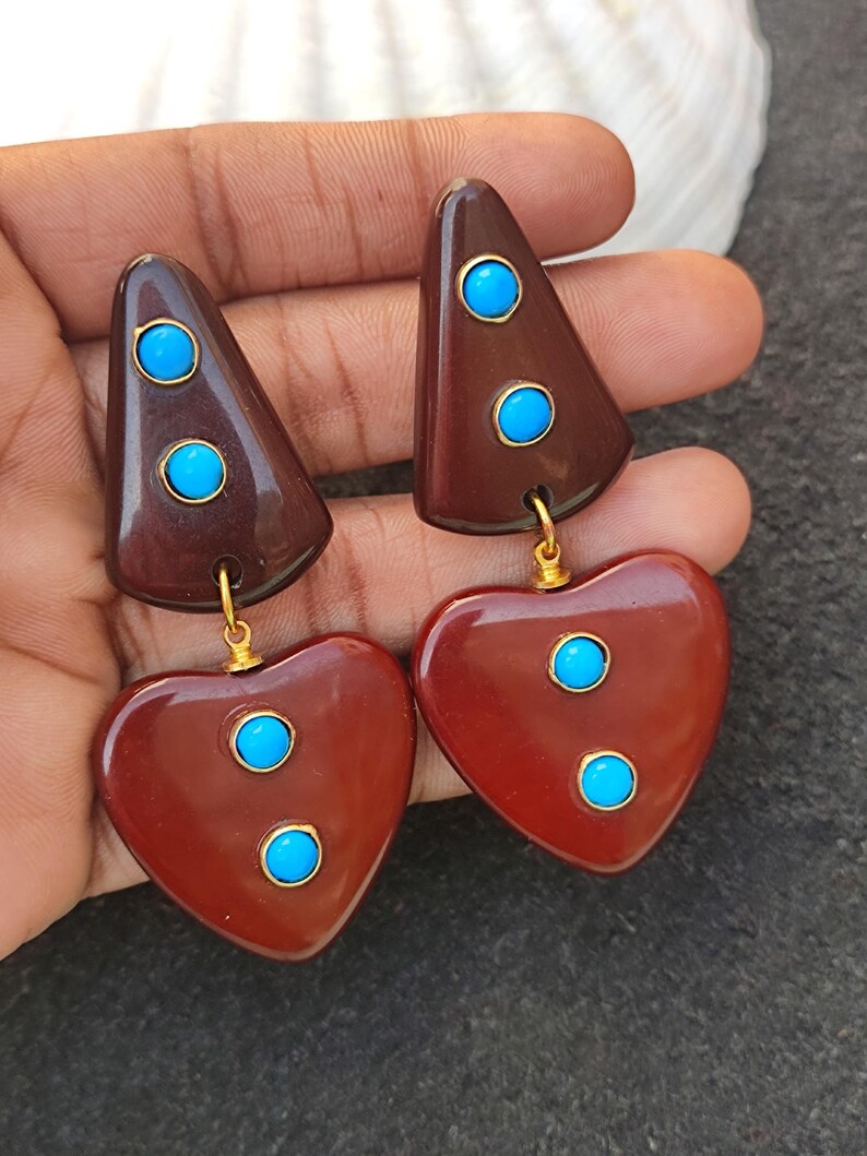 May include: A pair of brown and red heart-shaped earrings with turquoise stones. The earrings are made of resin and have a gold-tone finish.