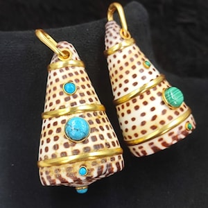 May include: A pair of cone-shaped earrings. The earrings are made from a spotted shell material, accented with gold-colored metal bands and turquoise and green gemstones. The earrings have a gold-colored hook for hanging.