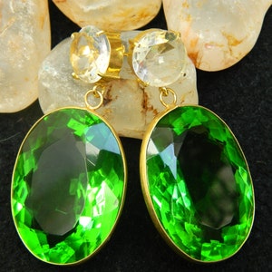 May include: A pair of gold earrings with green oval-shaped gemstones and clear round gemstones.