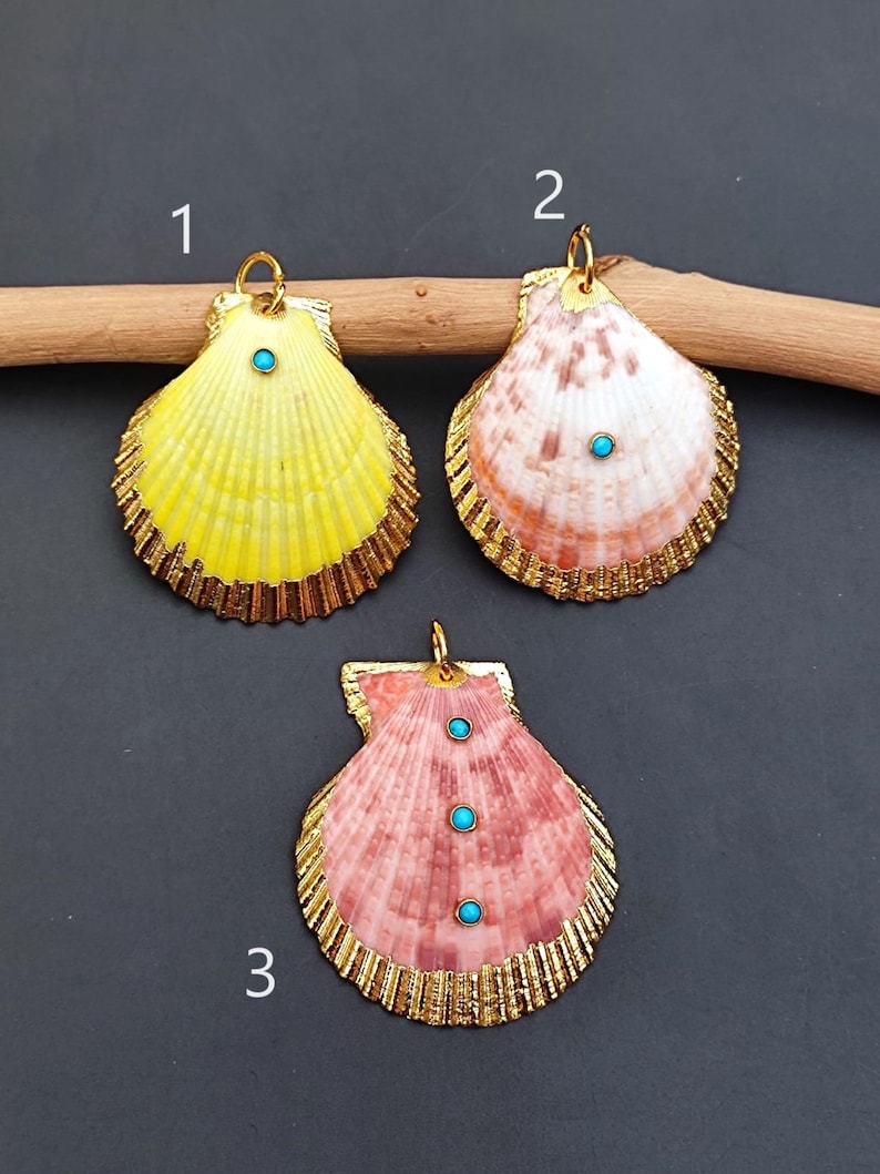 K&ouml;nnte beinhalten: Drei goldgerahmte Muschel Anh&auml;nger mit t&uuml;rkisfarbenen Steinen. Die Muscheln sind gelb, rosa und braun. Die Anh&auml;nger sind mit 1, 2 und 3 nummeriert.