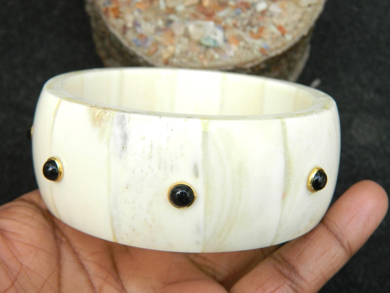May include: A white bone bangle bracelet with black gemstone accents. The bracelet is made of natural bone and has a polished finish.