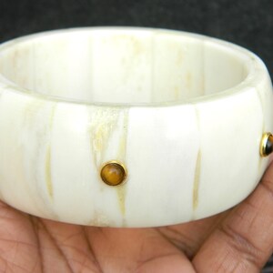 May include: White bone bangle bracelet with three gold-rimmed tiger's eye stones.