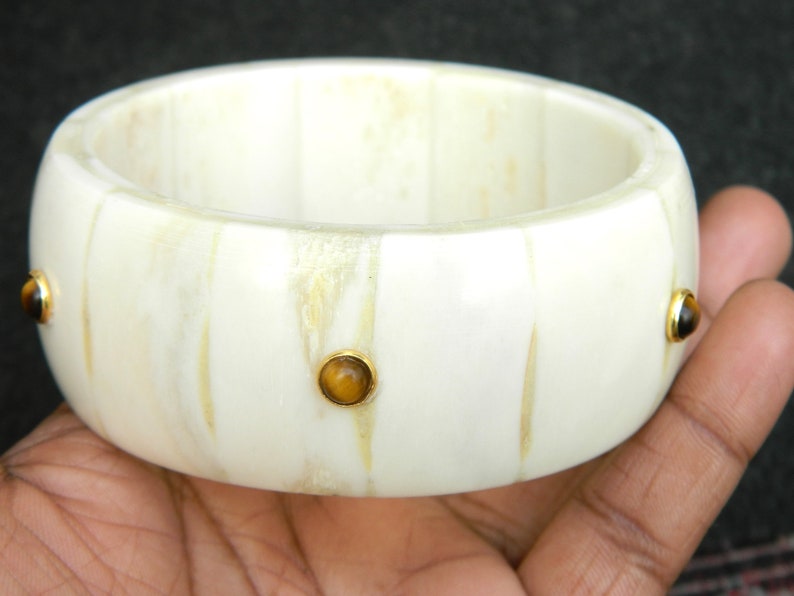 May include: White bone bangle bracelet with three gold-rimmed tiger's eye stones.