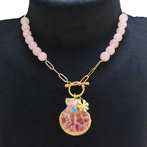 May include: A gold chain necklace with a pink stone bead strand and a gold seashell pendant with a turquoise stone and a gold flower charm.