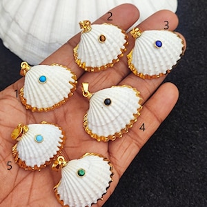 May include: Six white seashell pendants with gold trim and different colored gemstones in the center. The pendants are numbered 1 through 6.