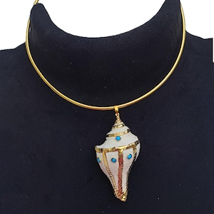 May include: A gold-colored choker necklace with a seashell pendant. The pendant is white with gold trim and small blue accents. The necklace is displayed on a black surface.