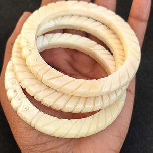 May include: Three ivory bangles with a carved, ridged design. The bangles are stacked on top of each other.