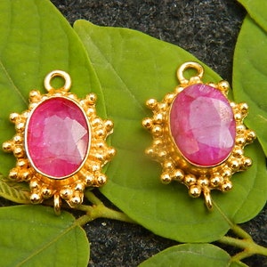 May include: Two gold-toned pendants featuring a pink oval gemstone set in the centre. Each pendant is encircled by a circle of small gold beads.