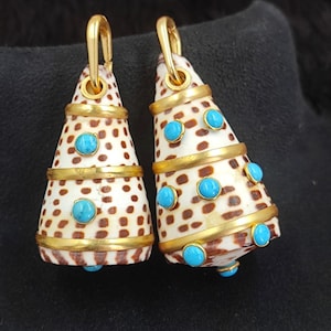 May include: A pair of cone-shaped earrings. The earrings are made from a spotted shell material, accented with gold-colored bands and turquoise-colored stones. The earrings have gold-colored hooks.