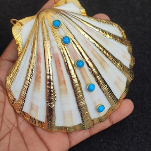 May include: A gold-painted seashell pendant with turquoise gemstones. The seashell is white with gold accents and has a natural texture.