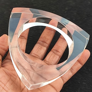 Peut inclure: Bracelet en acrylique transparent de forme triangulaire géométrique. Le bracelet présente un cercle intérieur arrondi et une finition lisse et polie. Le matériau transparent laisse passer la lumière, créant une esthétique moderne et minimaliste.