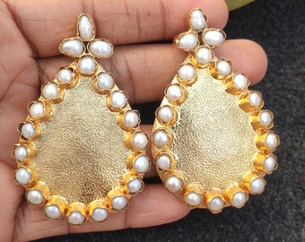 Peut inclure: Une paire de boucles d'oreilles en forme de larme de couleur or. Chaque boucle d'oreille présente un pendentif en forme de larme de couleur or entouré d'une bordure de perles blanches.