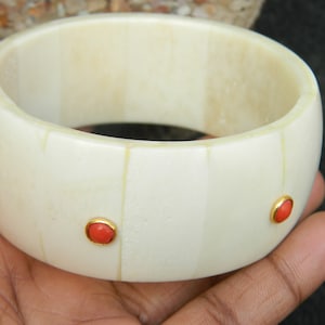 May include: White bone bangle bracelet with three red coral stones set in gold.