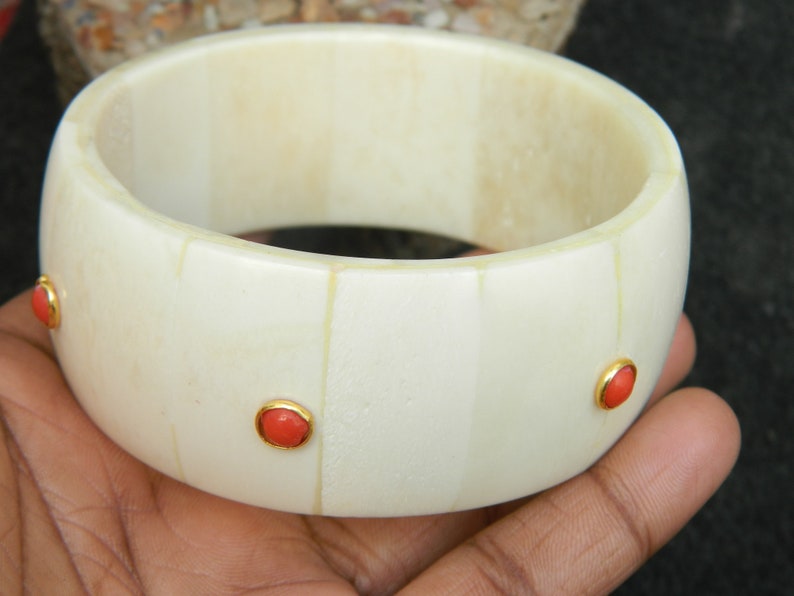 May include: White bone bangle bracelet with three red coral stones set in gold.