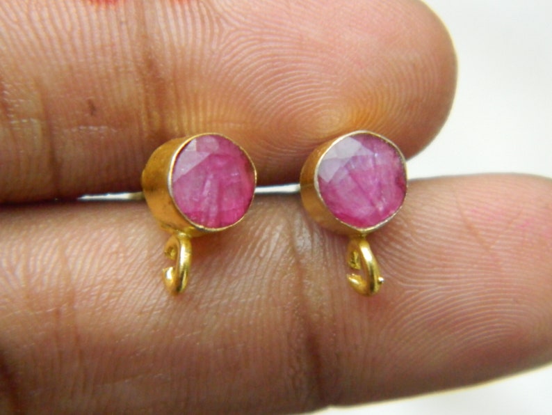 Pu&ograve; includere: Un paio di orecchini d'oro con accenti di pietre preziose rosa. Gli orecchini hanno un piccolo anello in basso.