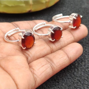 May include: Three silver rings with red gemstone settings. The rings are adjustable and have a simple design.