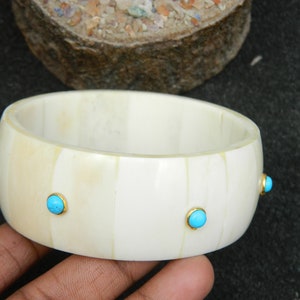 May include: White bone bangle bracelet with four turquoise blue stones set in gold.