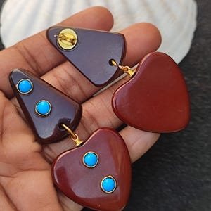 May include: A pair of dangle earrings with a brown heart and triangle shape. The earrings have turquoise accents.
