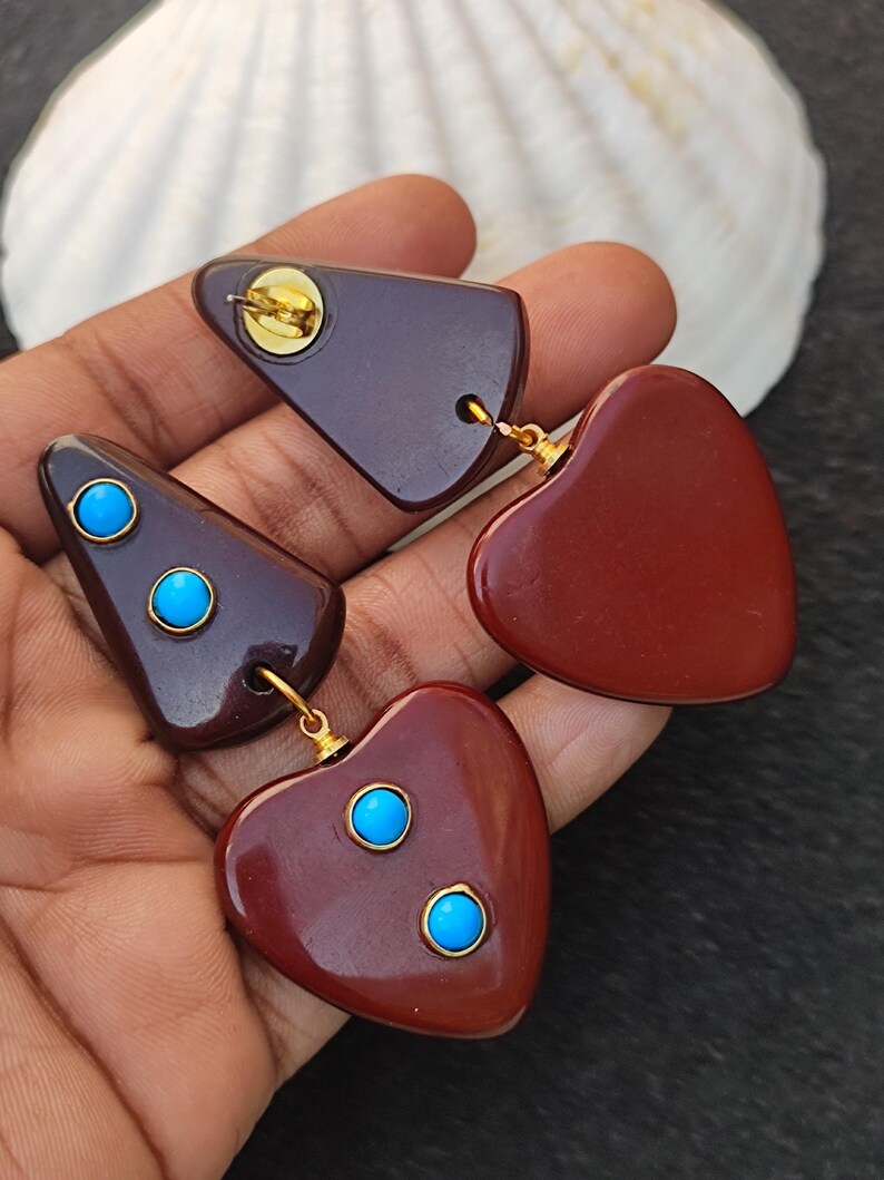 May include: A pair of dangle earrings with a brown heart and triangle shape. The earrings have turquoise accents.