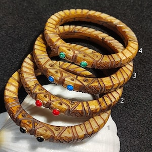 May include: Four stacked bone bangles with intricate carvings. Each bangle has two small gemstones: black, red, blue, and green.