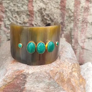 May include: A brown horn cuff bracelet with three oval-shaped green malachite stones set in gold.