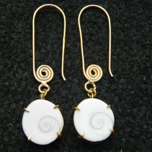 May include: A pair of gold earrings with white shell pendants. The shells have a spiral pattern and are set in a gold frame.