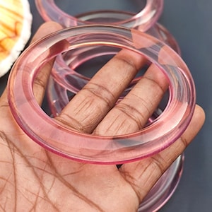Op de afbeelding: Set van vier roze doorschijnende armbandjes. De armbandjes zijn op elkaar gestapeld en gemaakt van een glad, glanzend materiaal.