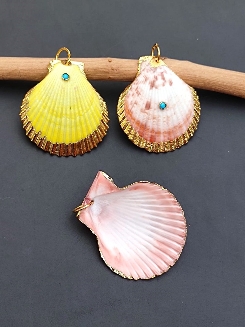 K&ouml;nnte beinhalten: Drei Muscheln mit goldenen Verzierungen und t&uuml;rkisfarbenen Akzenten. Die Muscheln sind in Gelb, Rosa und Wei&szlig; bemalt.