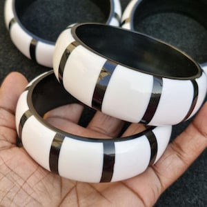 May include: Four black and white striped bangles. The bangles are made of a glossy material and have a wide, rounded shape.