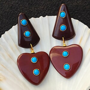 May include: A pair of brown heart-shaped earrings with turquoise stones. The earrings are made of resin and have a gold-tone finish.