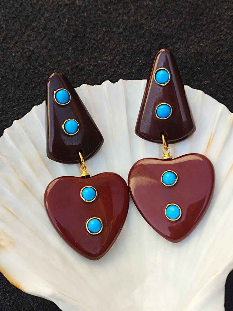 May include: A pair of brown heart-shaped earrings with turquoise stones. The earrings are made of resin and have a gold-tone finish.