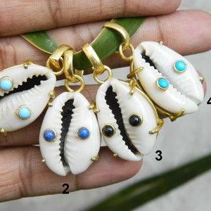 May include: Four gold cowrie shell pendants with different colored gemstones. The shells are white with gold accents and the gemstones are turquoise, blue, and black.
