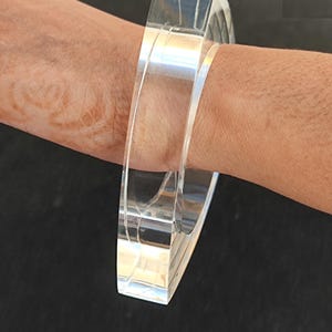 Op de afbeelding: Een heldere, rechthoekige acrylarmband. De armband is transparant en heeft een glad, gepolijst oppervlak. Het ontwerp is eenvoudig en modern, geschikt voor dagelijks gebruik. De armband is ongeveer 6,35 cm breed.