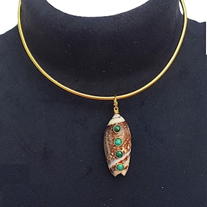 May include: A gold-tone choker necklace with a pendant. The pendant is an elongated shell shape with a brown and white pattern, accented with three green malachite stones. The necklace is displayed on a black surface.