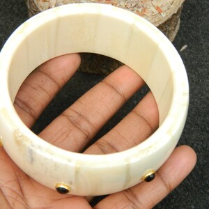 May include: A white bone bangle bracelet with three black gemstones set in gold.