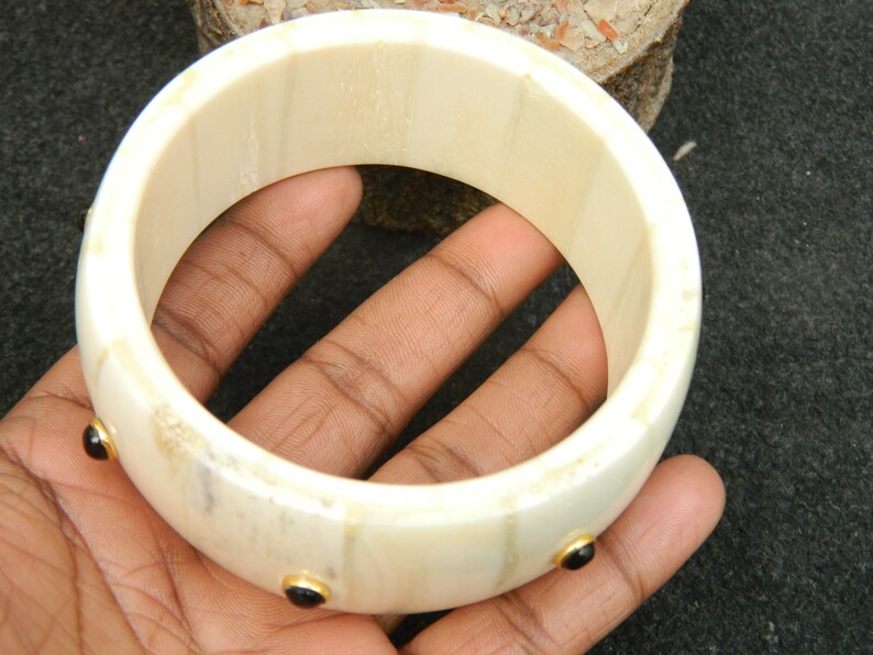 May include: A white bone bangle bracelet with three black gemstones set in gold.
