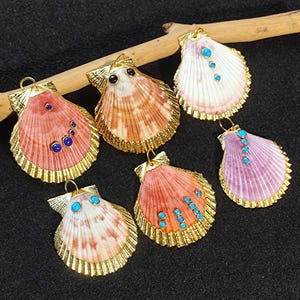 May include: Six scallop shell pendants with gold trim and blue and turquoise gemstones. The shells are various shades of pink, white, and purple.