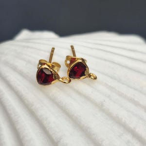 May include: A pair of gold earrings with small red heart-shaped gemstones. The earrings have a simple design and are perfect for everyday wear.