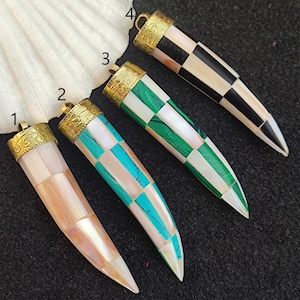 May include: Four decorative pendants made of inlaid mother of pearl in various colors and patterns. The pendants are shaped like a tooth and have a gold-colored metal cap at the top.